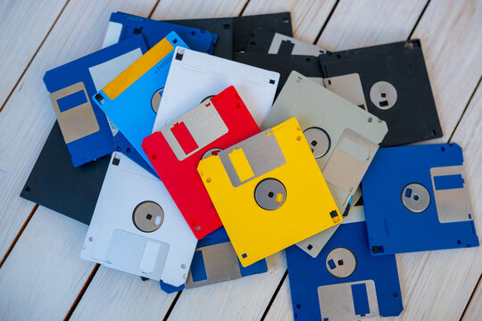 Colorful pile vintage 3.5 inch floppy disks on wooden surface, retro computing, obsolete data storage, tech nostalgia, digital history, collection old media formats 80s, 90s, nostalgic tech memory - Powered by Adobe