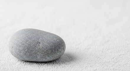 A single gray pebble rests on a textured white surface