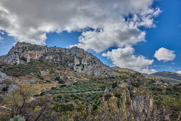 Obraz premium Rocky mountainside with olive groves under a cloudy sky