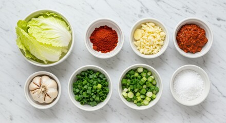 Overhead view of kimchi ingredients in white bowls on a white marble surface ready to cook