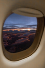 Fototapeta premium This is a vertical, close-up view through an airplane window (or porthole) capturing a vibrant sunset or sunrise above the clouds
