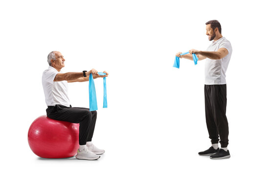 Sports coach showing an exercise with a resistance band to a mature man seated on a fitness ball