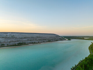Aerial view of turquoise waters of Auvere ash pond near Narva, Estonia, with rippled surface, quarry landscape, and greenery at sunset.