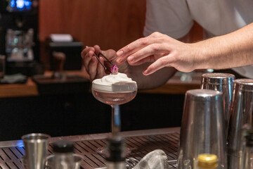 Bartender garnishing cocktail with whipped cream and decorative flower