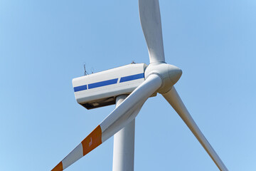 Close-up view of tall white wind turbine set against a bright blue sky