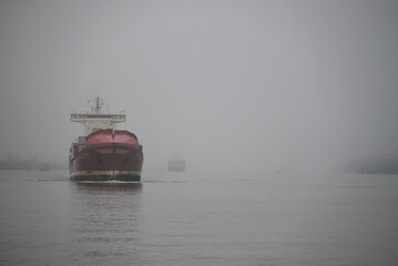 Vessels arrive at Hamburg Harbor on a foggy day. Crane, Vessel, River, Water. Hamburg Harbor, Hamburg, Germany