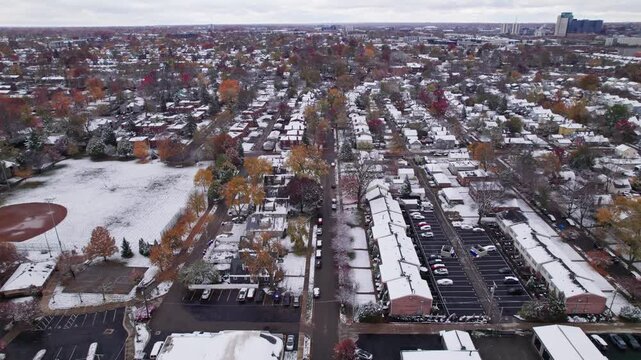 Drone shot and aerial view of Columbus, Ohio neighborhood homes, buildings, roads, buildings, and businesses during late fall after winter snowfall snow falling and colorful autumn trees and leaves up