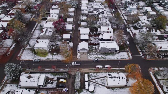 Drone shot and aerial view of Columbus, Ohio neighborhood homes, buildings, roads, buildings, and businesses during late fall after winter snowfall snow falling and colorful autumn trees and leaves up