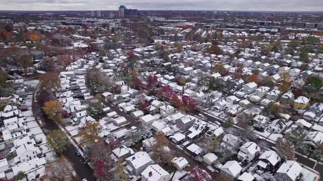 Drone shot and aerial view of Columbus, Ohio neighborhood homes, buildings, roads, buildings, and businesses during late fall after winter snowfall snow falling and colorful autumn trees and leaves up