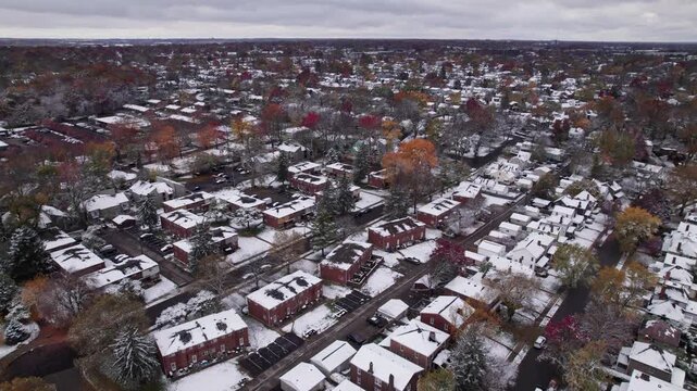 Drone shot and aerial view of Columbus, Ohio neighborhood homes, buildings, roads, buildings, and businesses during late fall after winter snowfall snow falling and colorful autumn trees and leaves up