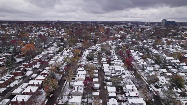 Drone shot and aerial view of Columbus, Ohio neighborhood homes, buildings, roads, buildings, and businesses during late fall after winter snowfall snow falling and colorful autumn trees and leaves up