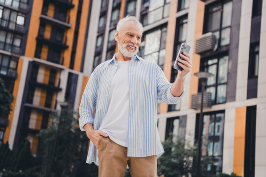Elderly man taking a selfie in a modern city residential complex on a sunny day suitable for lifestyle business urban outdoor photography