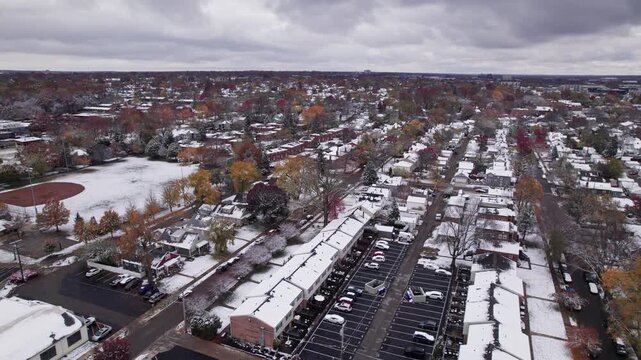Drone shot and aerial view of Columbus, Ohio neighborhood homes, buildings, roads, buildings, and businesses during late fall after winter snowfall snow falling and colorful autumn trees and leaves up
