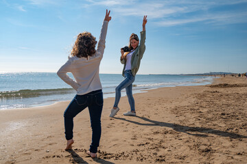 A girl is posing for a picture with her friend on the beach. The girl is wearing a white shirt and jeans