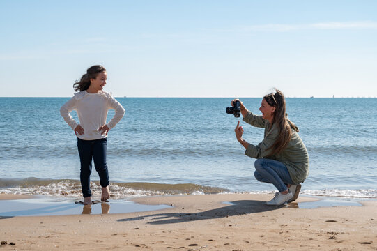 A girl is posing for a picture with her friend on the beach. The girl is wearing a white shirt and jeans - Powered by Adobe