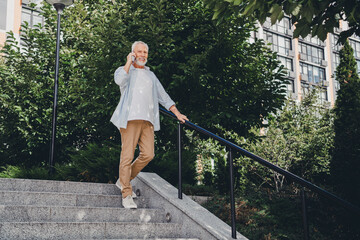 Elderly man on outdoor stairs talks on phone beside modern residential buildings in a sunny urban park setting conveying lifestyle real estate and everyday urban life