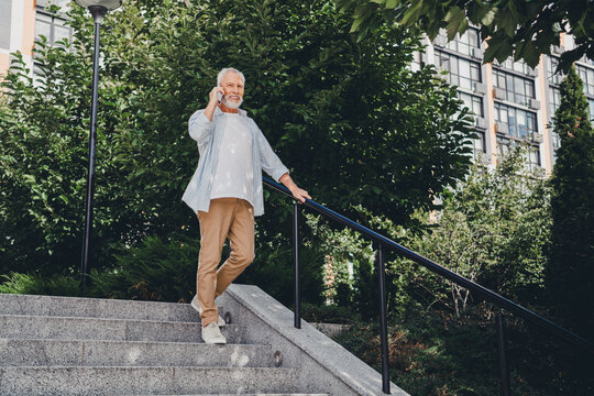 Elderly man on outdoor stairs talks on phone beside modern residential buildings in a sunny urban park setting conveying lifestyle real estate and everyday urban life