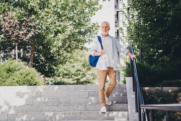 Elderly man with blue backpack walking down stairs in an urban park setting showcasing casual style and city life