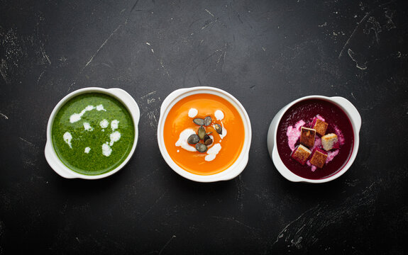 Three different bowls of healthy cream soups, green, orange pumpkin, and red beet, with fresh ingredients - Powered by Adobe