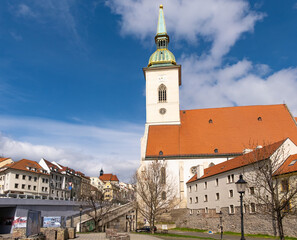 Fototapeta premium St. Martin's Cathedral stands prominently against the Bratislava skyline, showcasing its historical architecture. Nearby buildings and a clear sky add to the urban landscape's charm