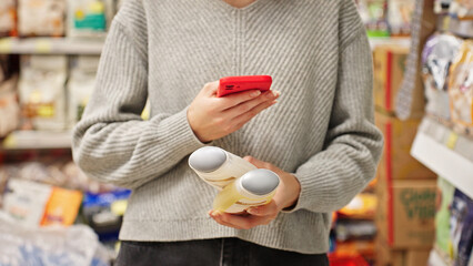Woman scanning dog shampoo with smartphone in pet store. Responsible pet owner comparing pet care products. Customer choosing pet grooming product, checking information, ingredients using mobile app