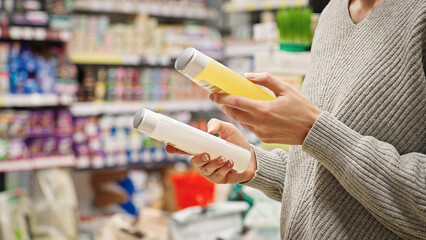 Woman comparing dog or cat shampoo in pet store. Responsible pet owner choosing pet care products. Customer reading the label and checking ingredients before purchase, choosing pet grooming product.