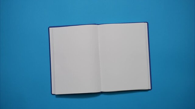 Opening a Blue Book on a Blank Page on Blue Background. Top View of the Opening Blank Diary Book. Stop Motion