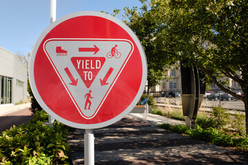 Red trail courtesy yield sign on a metal post along a walking path with instructions