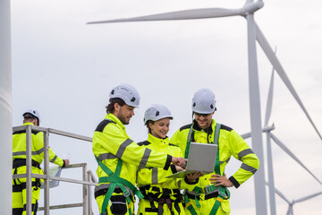 Three people wearing yellow safety gear are looking at a laptop. One of them is wearing a hard hat. Professional workers collaborating on renewable energy project, focusing on safety and maintenance.