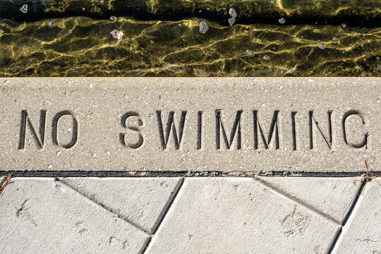 No swimming text warning stamped in cement beside water