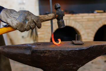 Blacksmith hammering glowing metal while forging hook