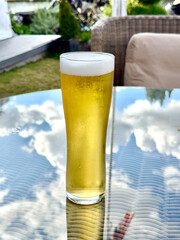 Pint glass of cold golden lager beer on a table in the garden of a luxury hotel. No people.