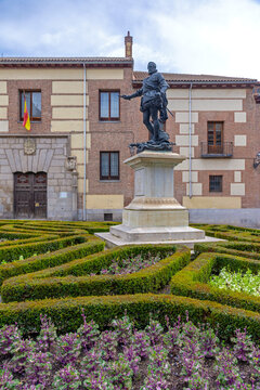 A close-up of the bronze statue of Don &Aacute;lvaro de Baz&aacute;n on an inscribed pedestal in Madrid's Plaza de la Villa, framed by a hedge and the historic red-brick buildings