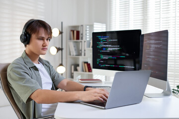 Programmer in headphones working on laptop at white table in office