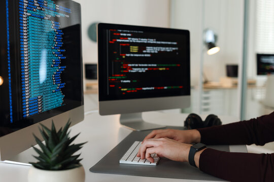 Programmer working on computer with dual monitors at white table in office, closeup