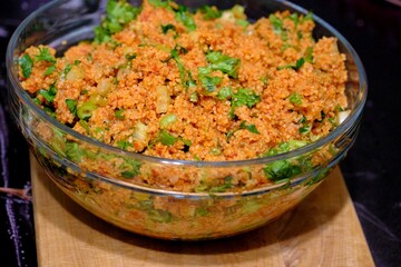 An image of kısır made with homemade bulgur in a glass bowl. Lettuce, green onions, and parsley are added to the kısır. Traditional Turkish food. Vegan diet. Snack plate.