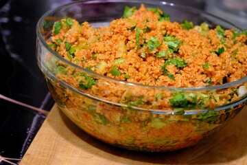 An image of kısır made with homemade bulgur in a glass bowl. Lettuce, green onions, and parsley are added to the kısır. Traditional Turkish food. Vegan diet. Snack plate.