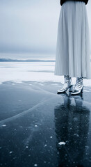 A surreal high-fashion scene of a woman in futuristic silver boots and a flowing pleated skirt standing on a vast, frozen lake. An ethereal and cold winter concept with dramatic reflections
