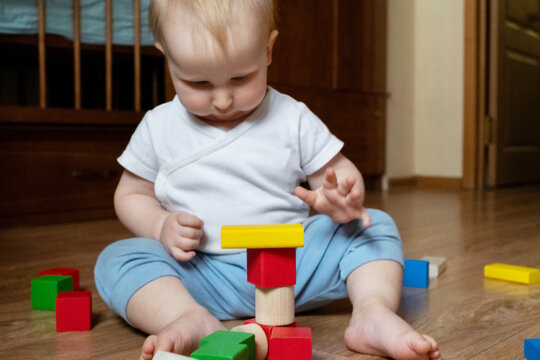 Child engaged in playing with eco-friendly wooden blocks on a floor. Focusing on hand-eye coordination and motor skills development through stacking activity. Ideal for educational content.