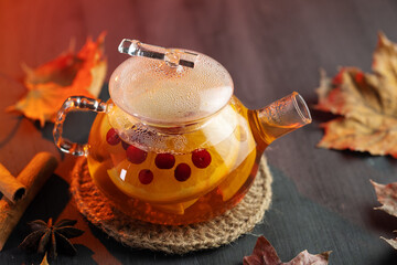 Tea with red berries, orange and spices in a teapot on a wooden table with autumn dry leaves