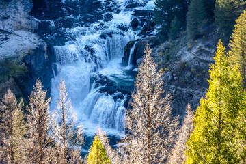 Sunlight catches the spray of the falls, creating a rainbow above the rushing river.