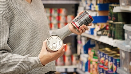 A woman choosing canned dog or cat food at a pet store, reading the label. Customer compares wet dog or cat food in the aisle with various canned goods on the shelves. Concept of responsible pet owner