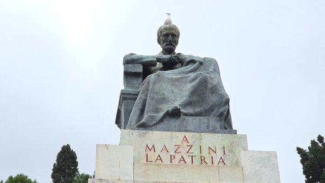 Rome, Italy – 11 January 2025. A statue of Giuseppe Mazzini seated with folded arms, a seagull on his head, and a marble pedestal bearing a red-lettered patriotic inscription.