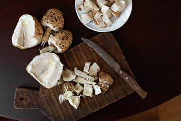 Macrolepiota procera, the parasol mushrooms, sliced on a dark board with plate and knife nearby. Concept of home cooking, rustic preparation, organic lifestyle. © Natallia