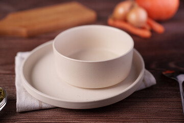 minimalistic kitchen scene featuring white ceramic bowl and plate on wooden table with blurred vegetables in background, creating a warm and rustic ambiance, fresh, culinary, aesthetic, earthy