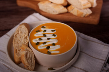 rich pumpkin soup topped with pumpkin seeds and cream, served with fresh sliced baguette on a rustic wooden table setting, refreshing, savory, tempting, charming, calm, elegant, luxurious, light