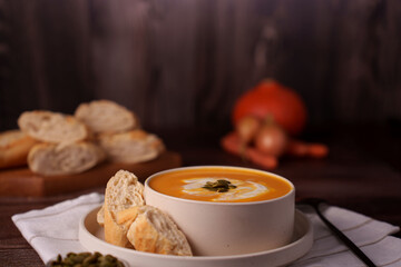 warm and inviting autumn scene with a bowl of creamy pumpkin soup garnished with seeds, served alongside crusty bread slices on a rustic wooden table, evoking a cozy, homely ambiance, peaceful