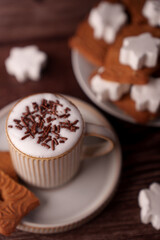 close-up of a frothy cappuccino topped with chocolate sprinkles in an elegant cup, accompanied by star-shaped frosted cookies on a wooden table for a cozy winter treat, presentation, aesthetic