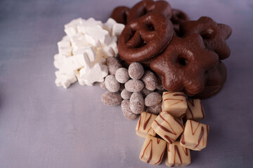 assorted confectionery arrangement with chocolate-covered pretzels, marshmallow stars, sugar-coated almonds, and vanilla fudge on textured purple background, display, casual, relaxing, appetizing