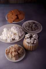 cozy dessert arrangement with hot cocoa topped with marshmallows, assorted biscuits and sweets on plates against subtle purple background, subtle, softlight, interior, layout, abundance, plethora